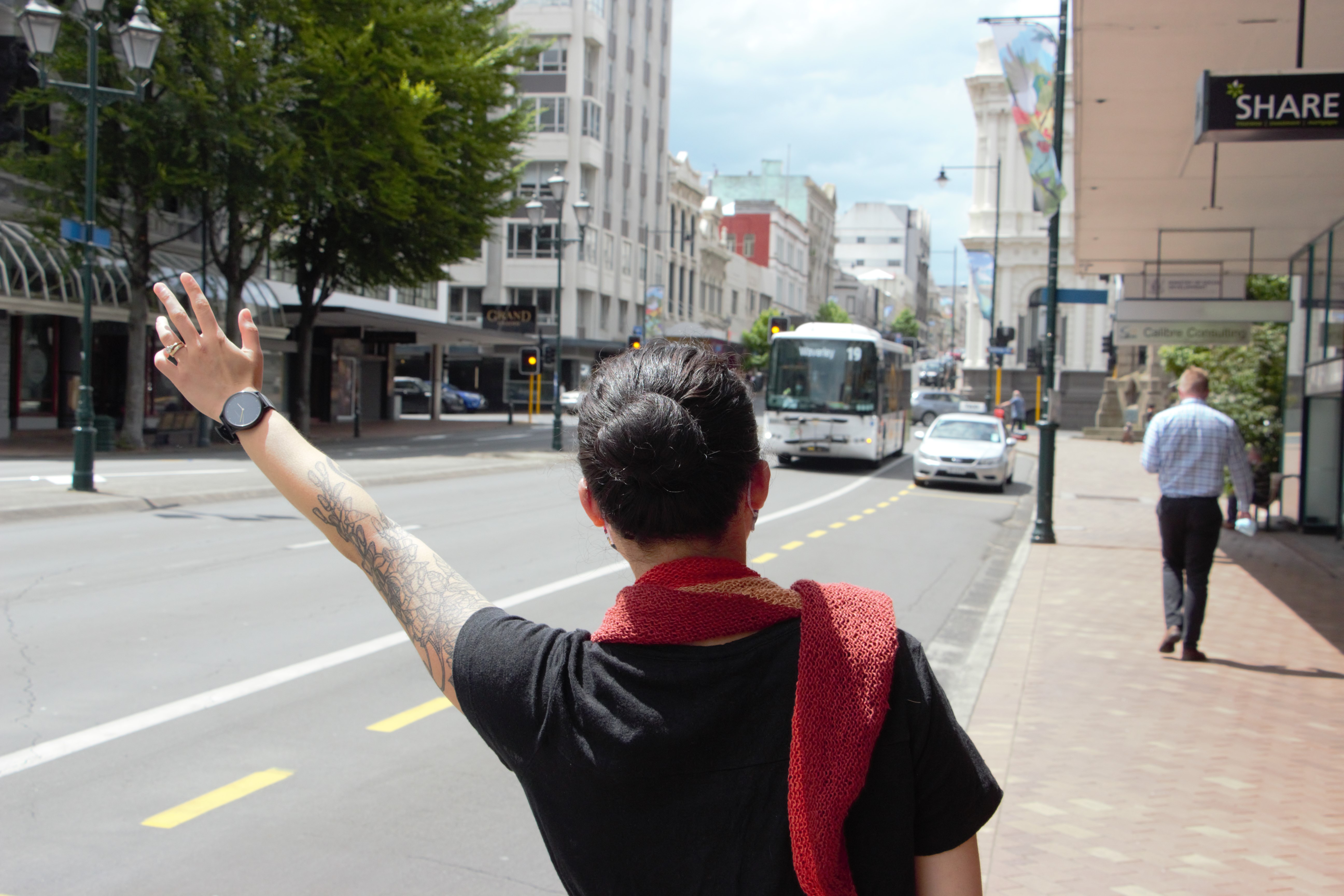 Person with left arm raised to single the oncoming bus to stop