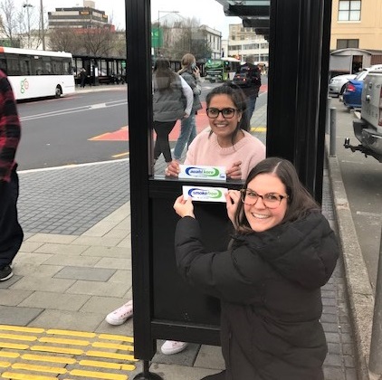 Pictured are Komal Suratwala (at back) and Catherine Thomas, Public Health South Health Promotion Advisors putting up stickers at the Bus Hub.