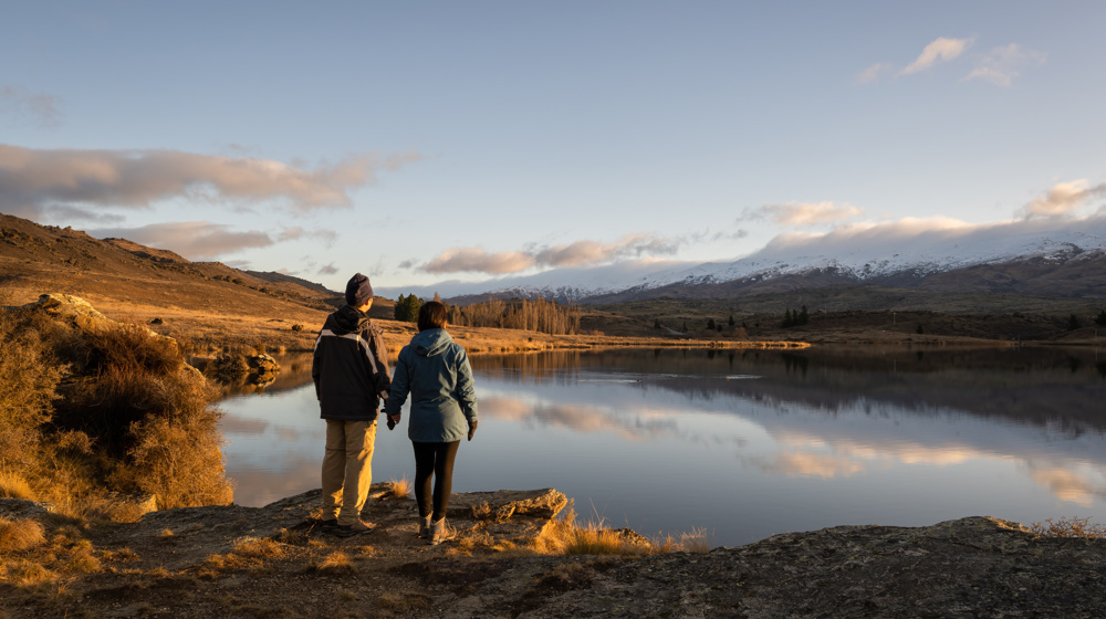 Butchers Dam Couple Watching The Sunset Flat Top Hill Conservation Reserve, Alexandra, Central Otago. Adobestock 527782796