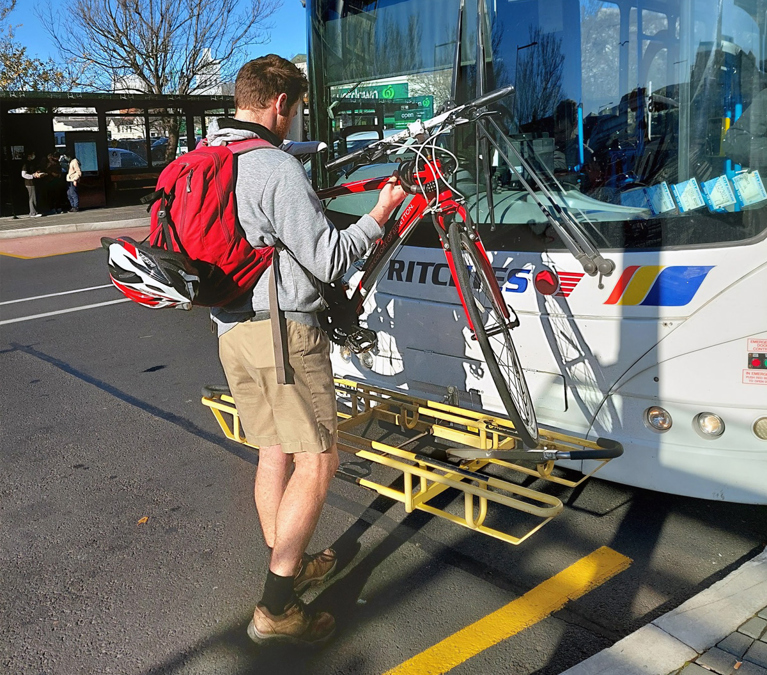 A young man loads his bike onto the bus via the front bike rack.